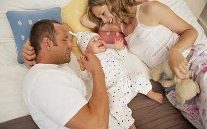 Parents lying either side of baby boy (8-12 months) smiling